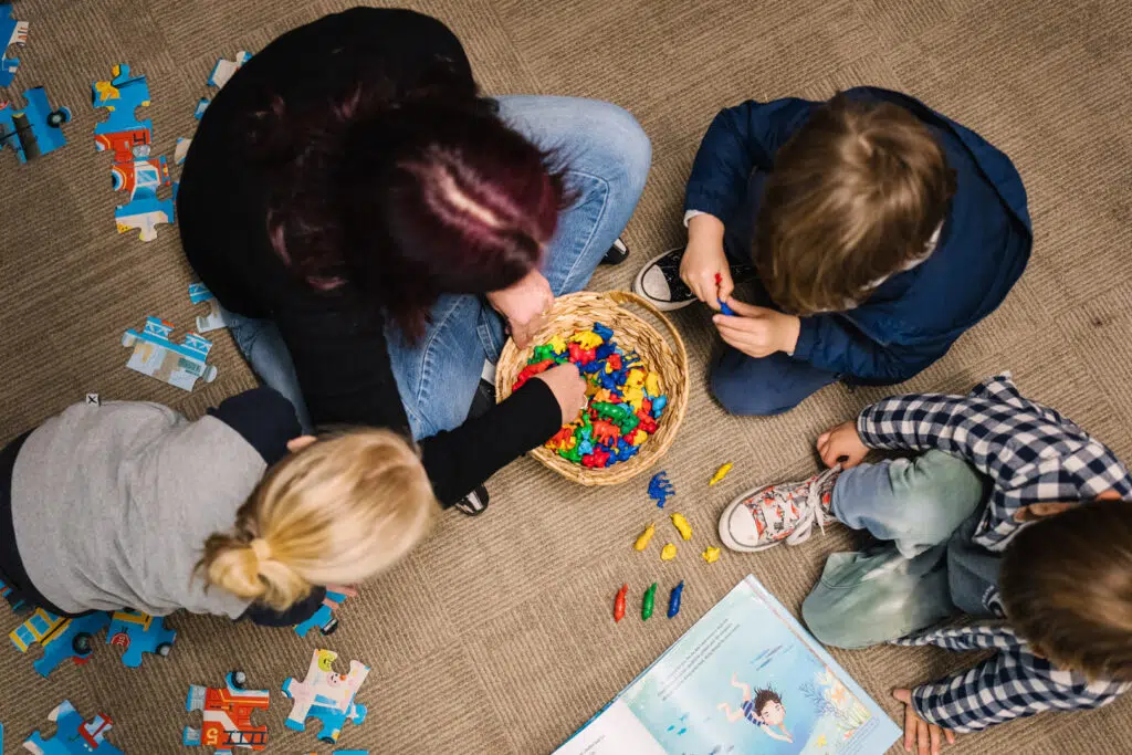 KU Bulli childcare educator and children playing with colourful plastic animals