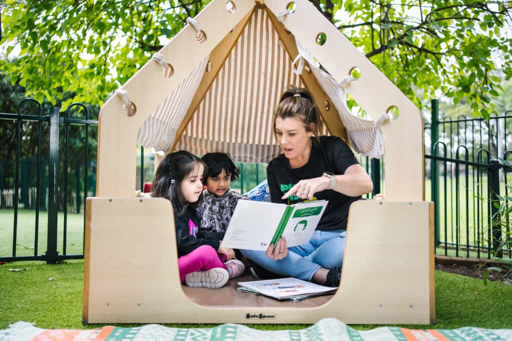 KU Macquarie Fields childcare educator reading a story to children in a cubby house