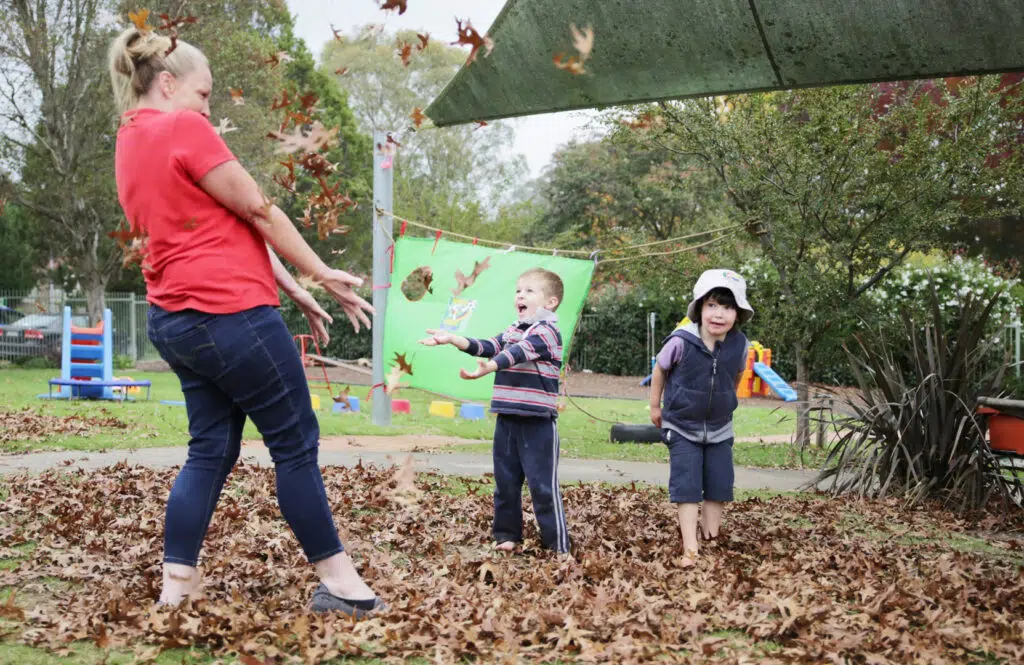 KU Moss Vale childcare educator and children having fun with Autumn leaves