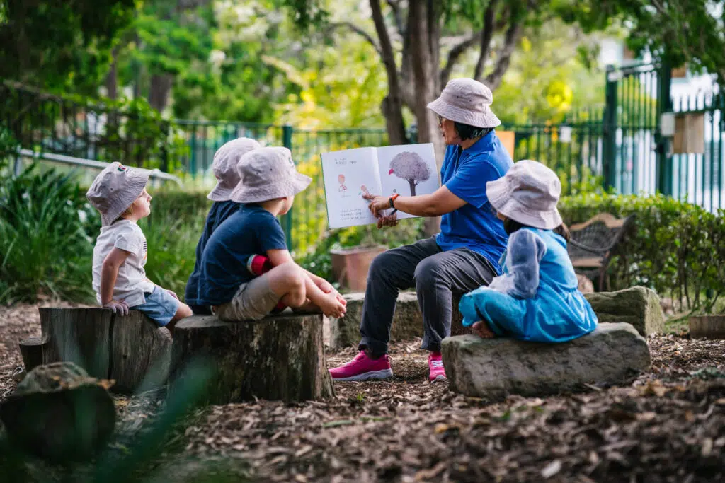 KU Rushcutters Bay childcare educator reading a story to children outdoors