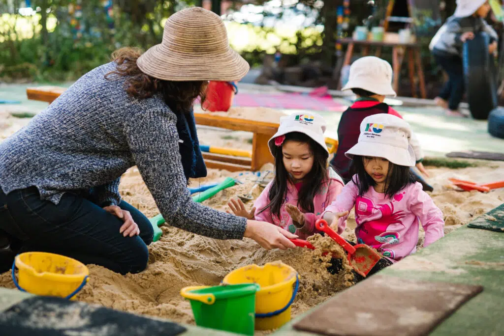 KU Henson Street childcare educator helping children build sandcastles