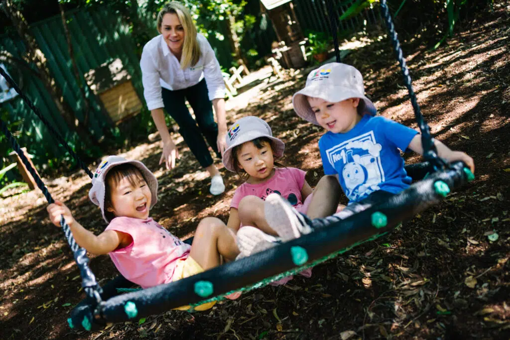 KU Bradfield Park childcare educator pushing some children on a swing