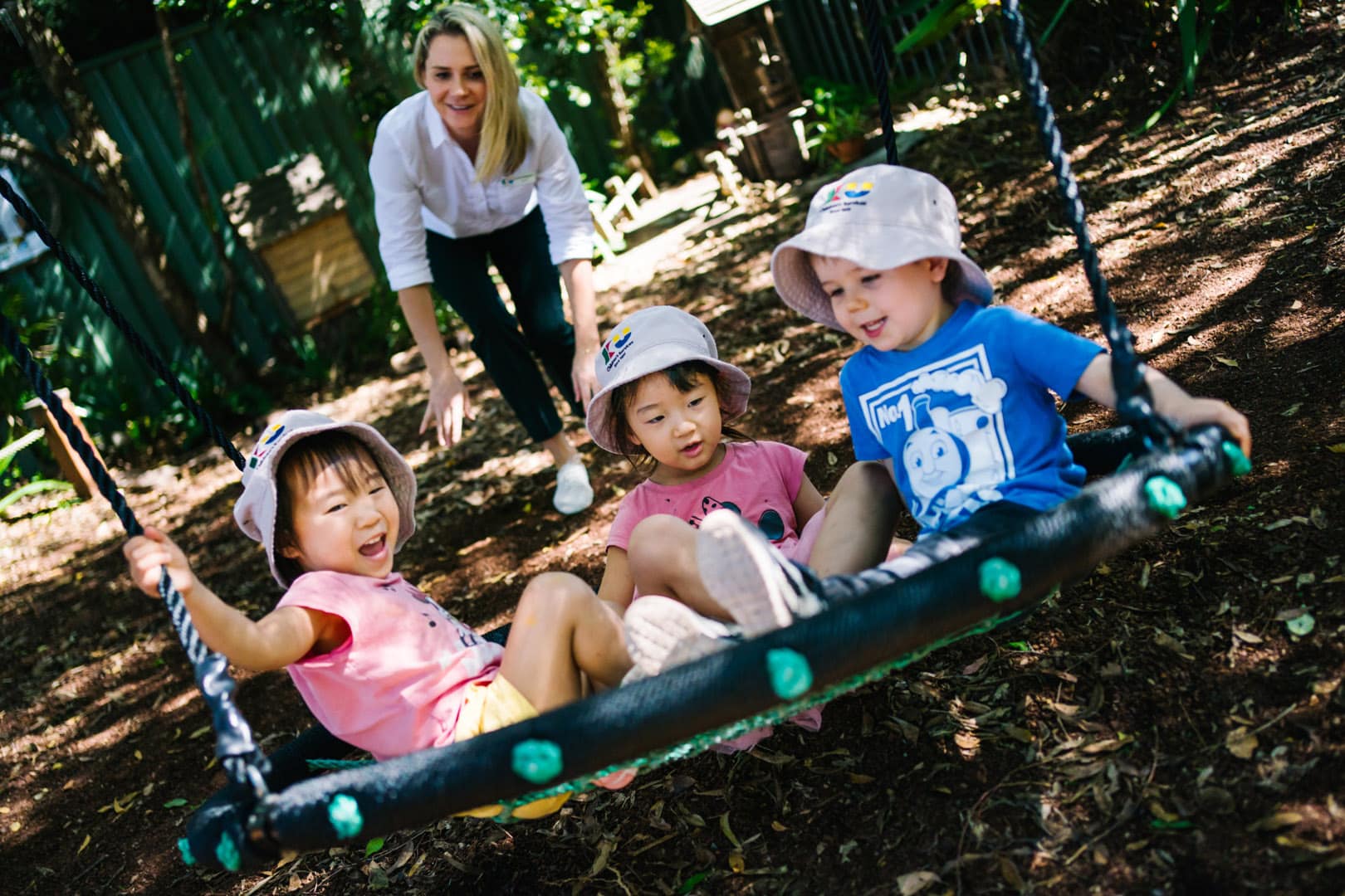 KU Bradfield Park childcare educator pushing some children on a swing